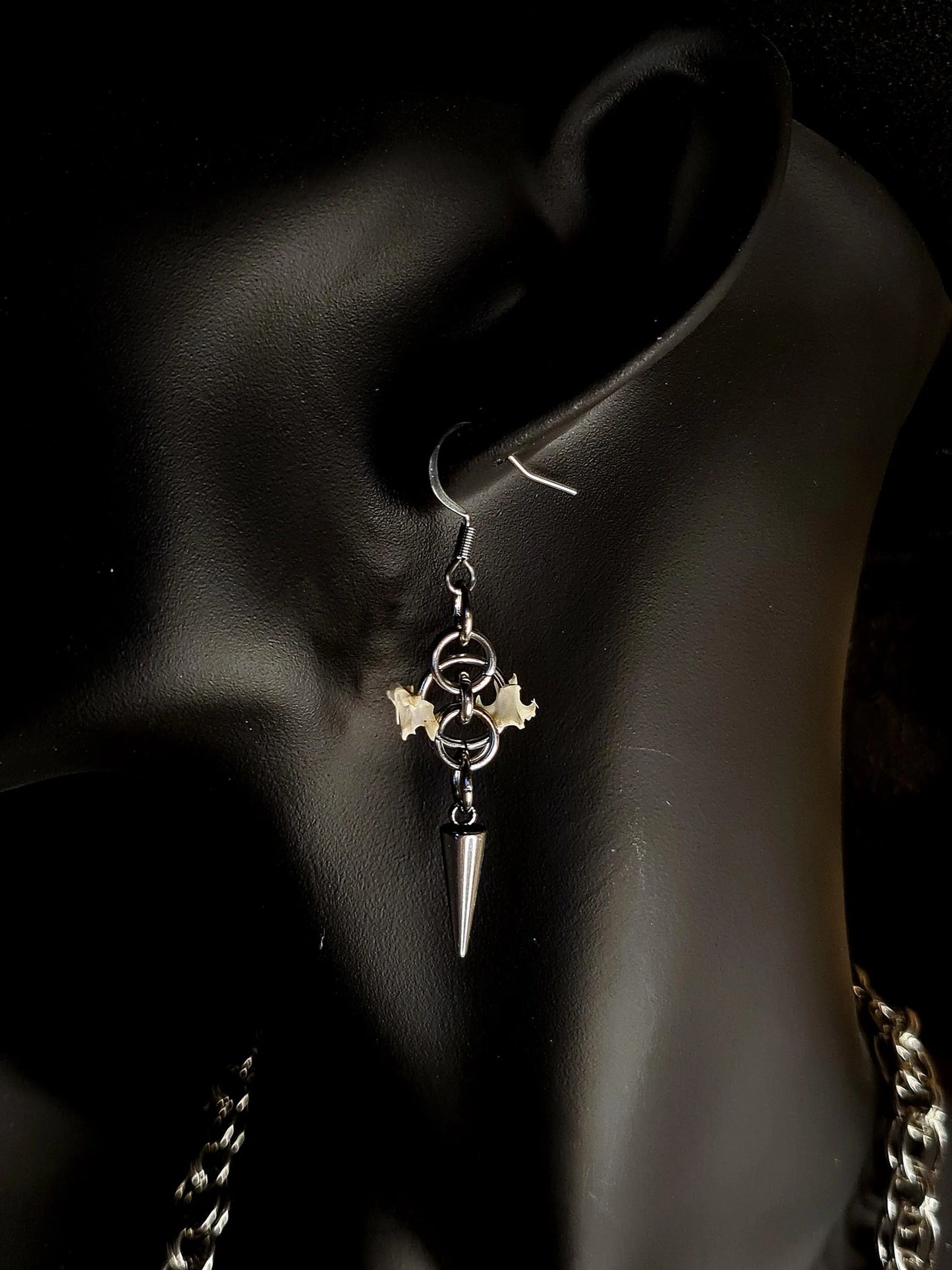 Earring with a spike and circular design encasing two bird bone vertibrae worn on an ear against a dark background