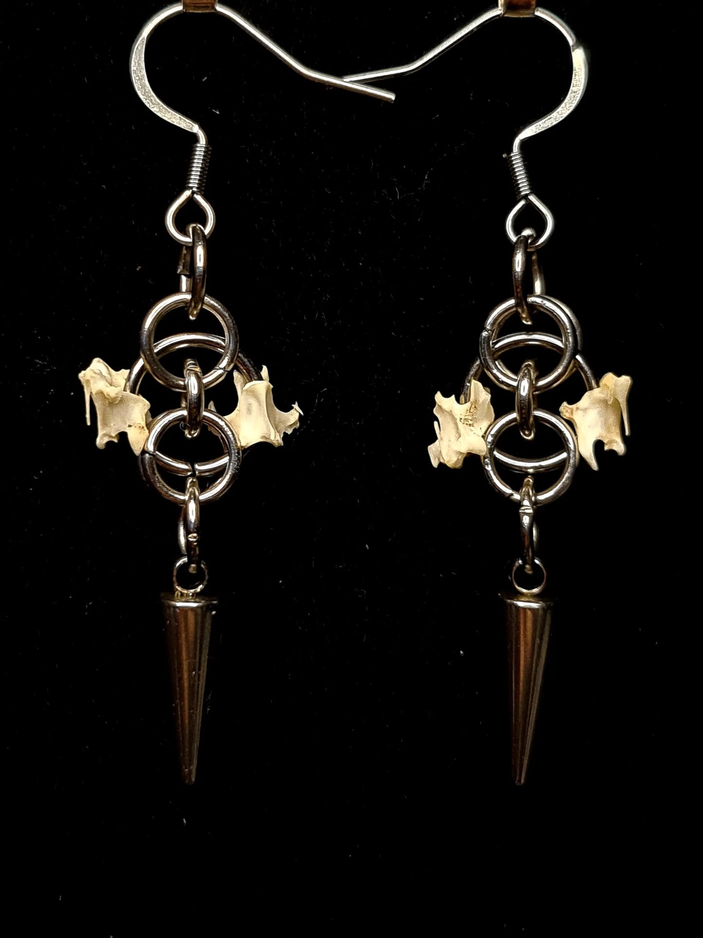 Pair of earrings with bird bones and spikes on a black background