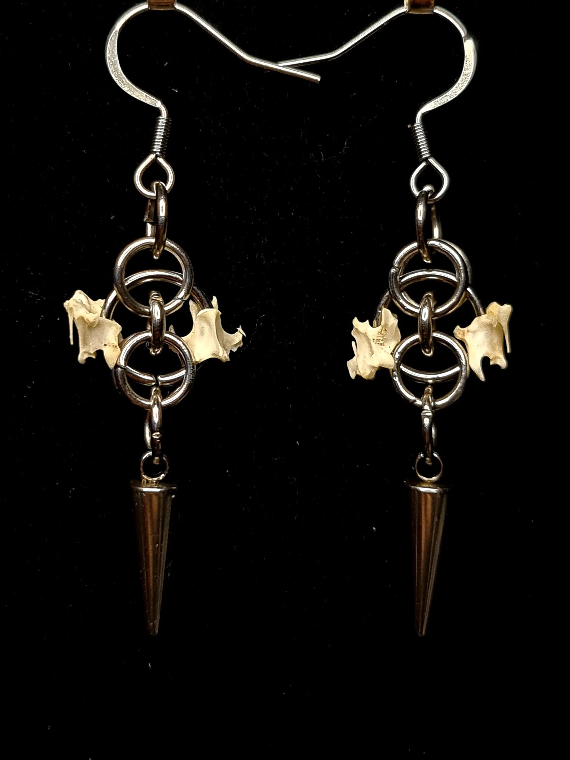 Pair of earrings with bird bones and spikes on a black background