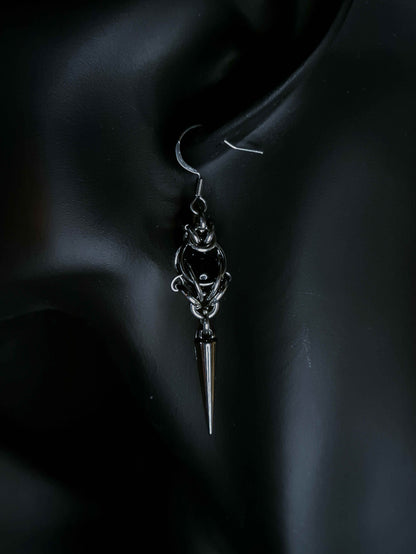 Silver earring with a pointed design on an ear against a dark background
