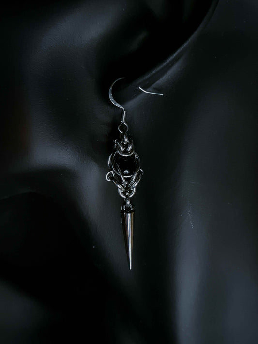Silver earring with a pointed design on an ear against a dark background