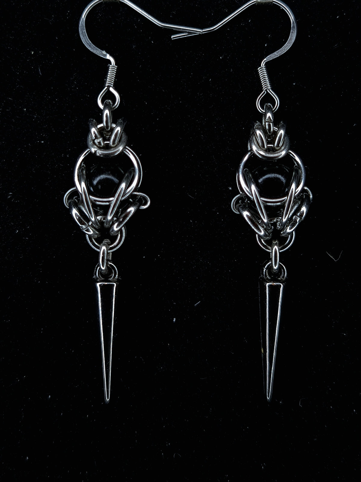 Pair of silver earrings with a central circular design and a pointed spike on a black background