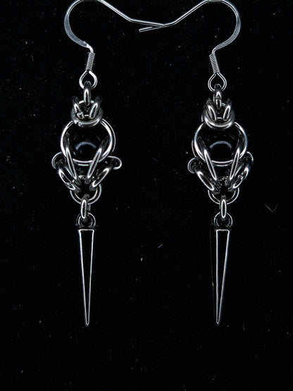 Pair of silver earrings with a central circular design and a pointed spike on a black background