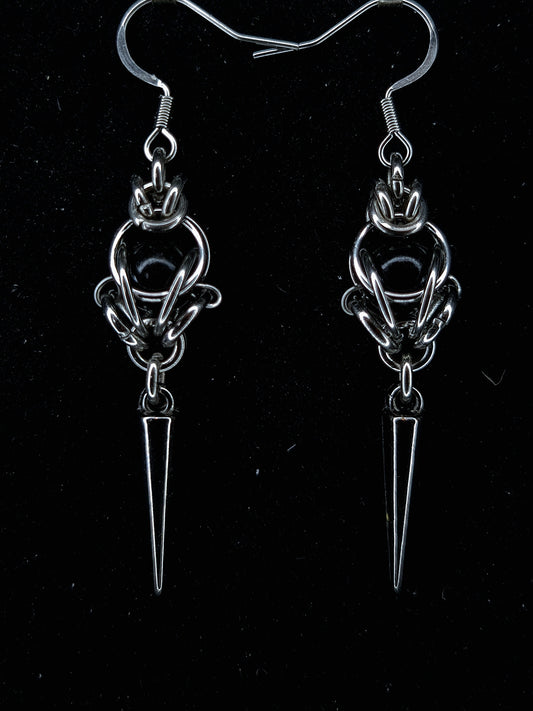 Pair of silver earrings with a central circular design and a pointed spike on a black background