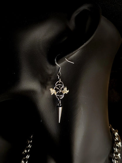 Earring with a spike and circular design encasing two bird bone vertibrae worn on an ear against a dark background