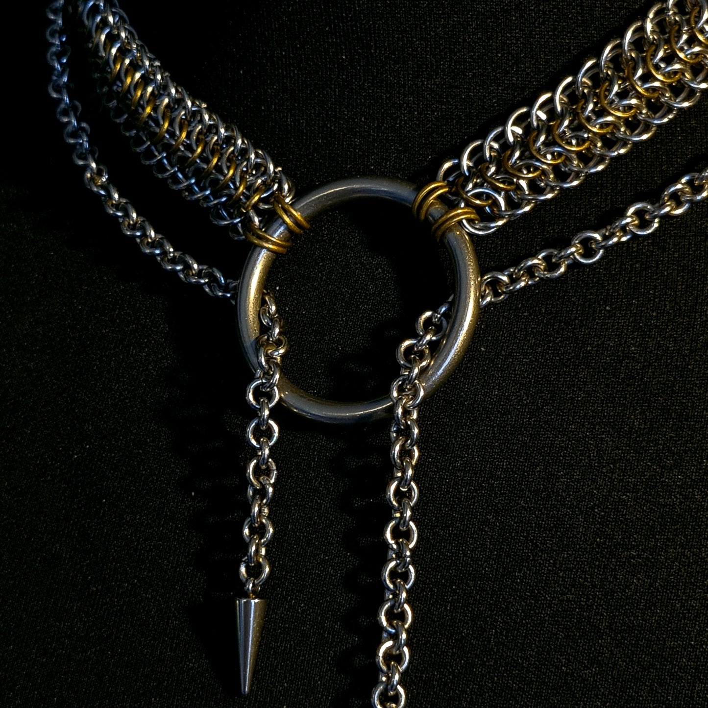 Close-up of a metallic necklace with a ring and spike on a black background