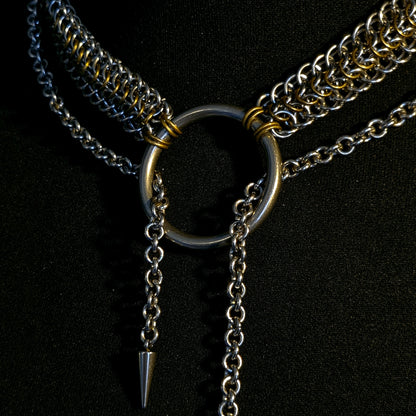 Close-up of a metallic necklace with a ring and spike on a black background