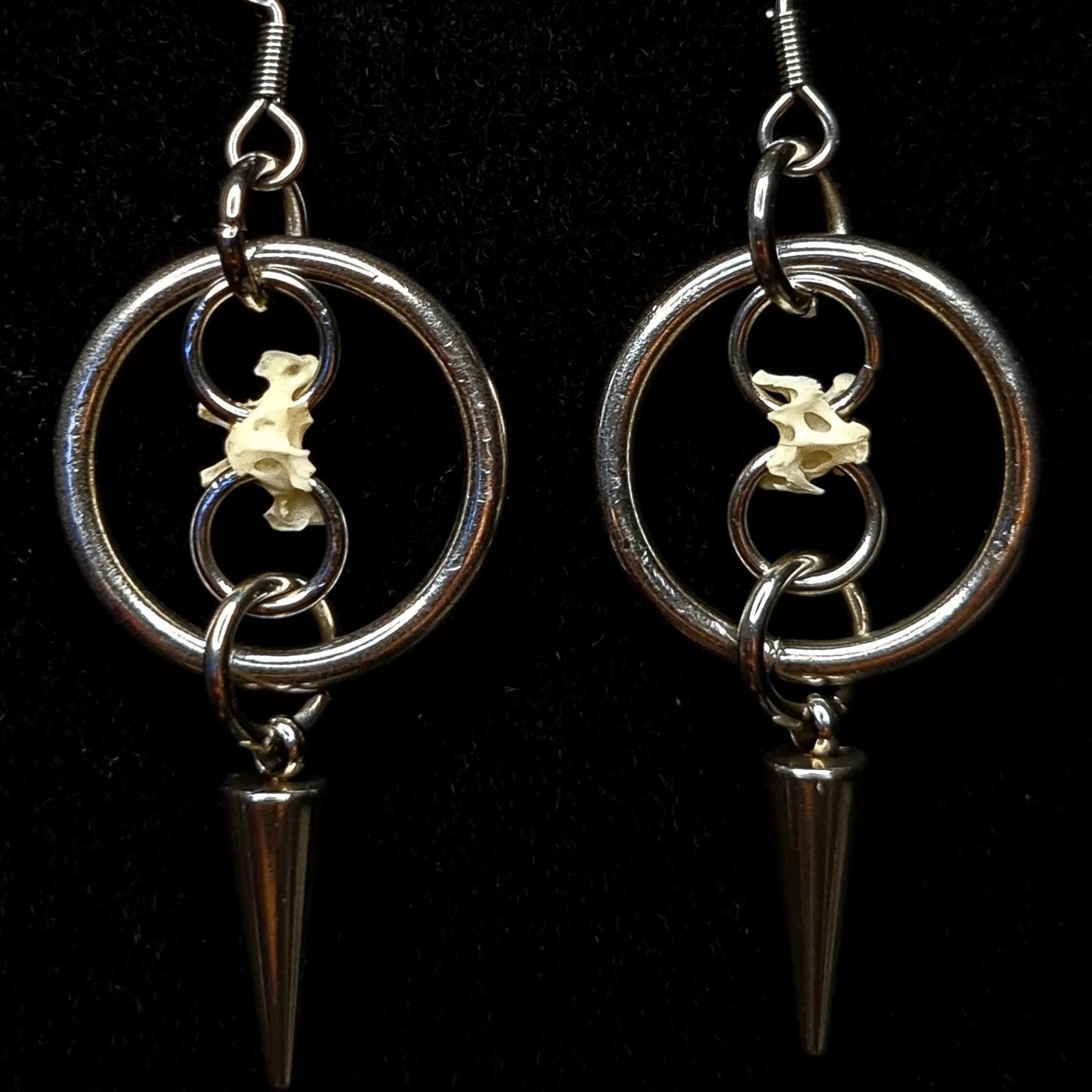 Two O ring hoop earrings with spikes and chains holding bones on a black background