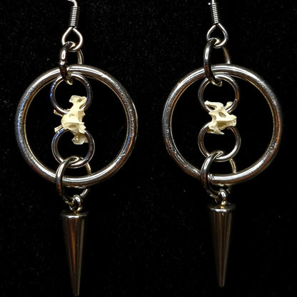 Two O ring hoop earrings with spikes and chains holding bones on a black background