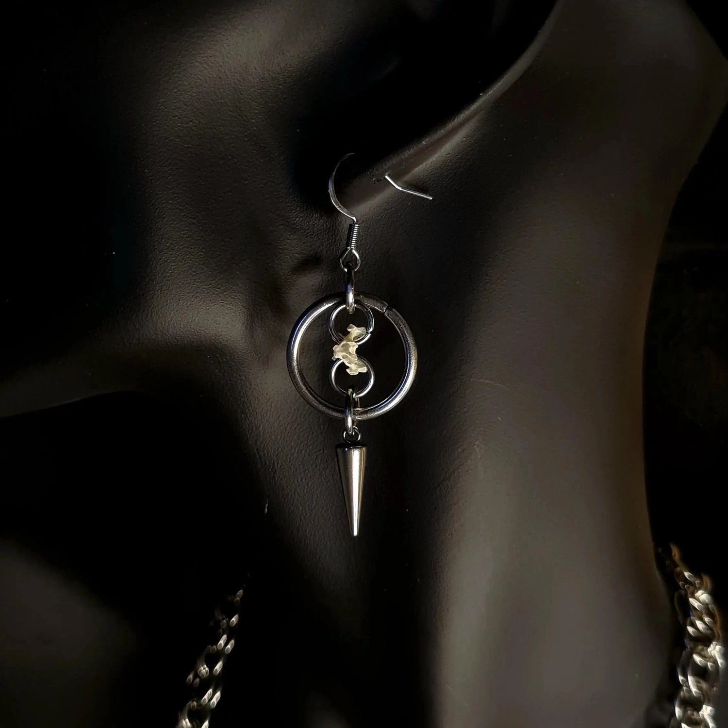 O Ring surrounding a chain holding a spine bone with a spike on an earring and black background