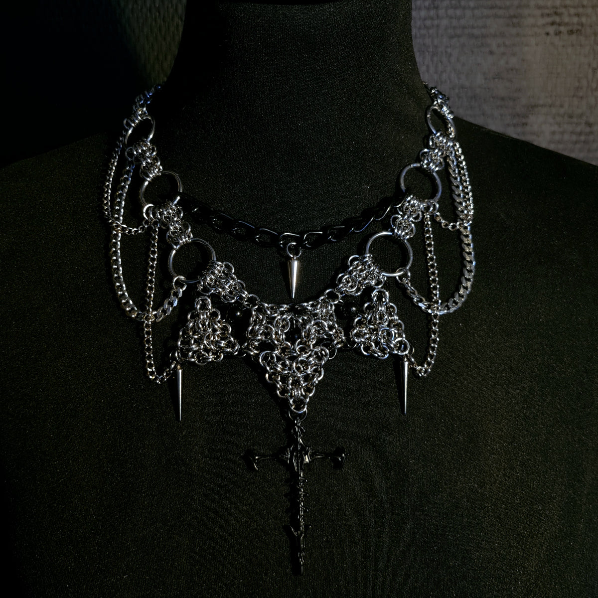 Gothic-style necklace choker with chains and spikes and cross on a black background