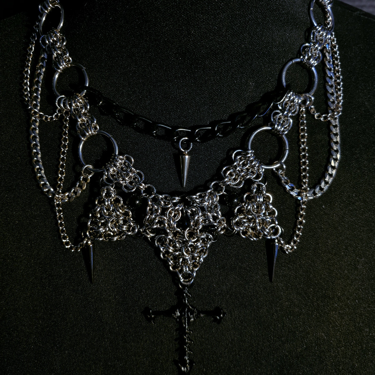 Gothic-style necklace with chains, spikes, and cross pendant on a black background