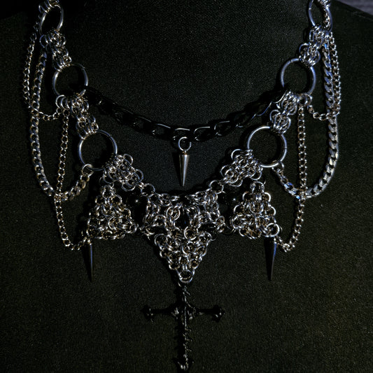 Gothic-style necklace with chains, spikes, and cross pendant on a black background