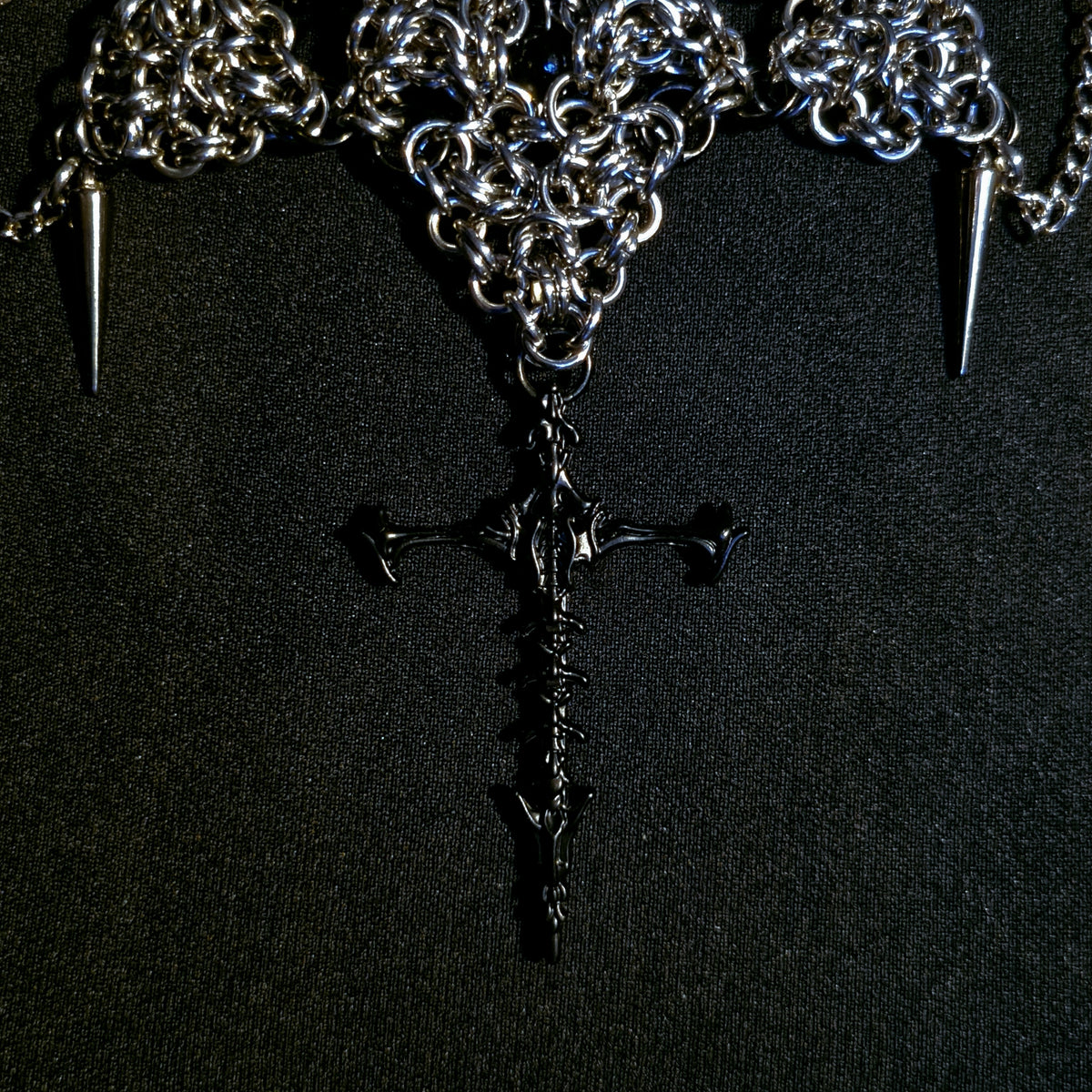 Necklace with chain, spikes, and a black spine cross pendant on a black background