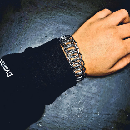 Chunky chainmail bracelet on wrist with black sleeve on dark background in punk image style